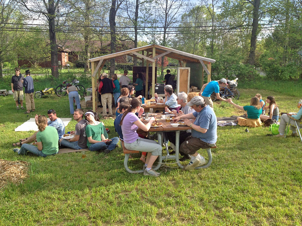 Photo of large group of people eating outside at picnic tables and sitting on the ground